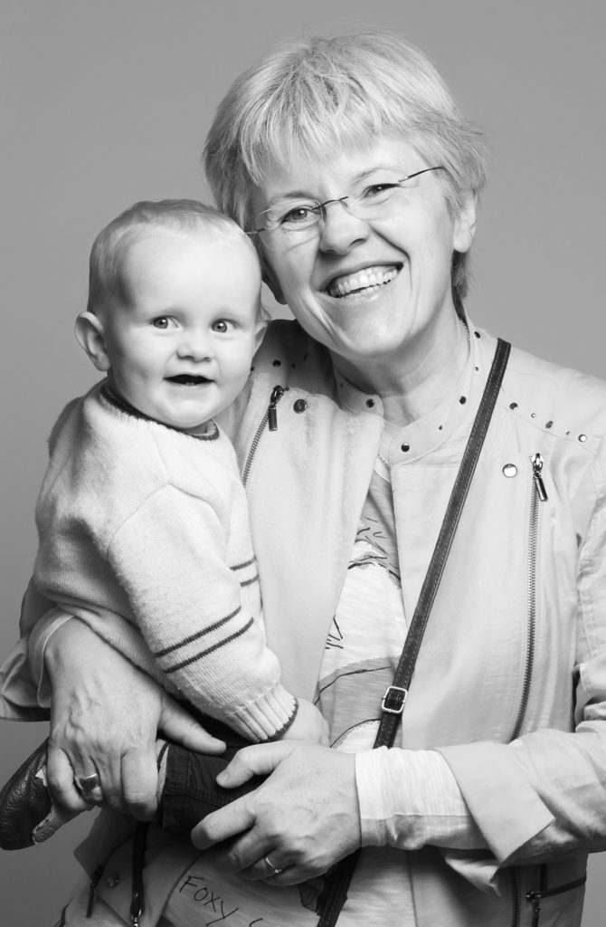 Charmantes Familienportrait vom Fotostudio Reuther, das eine Oma und ihr Enkelchen zeigt, die beide in die Kamera lachen.