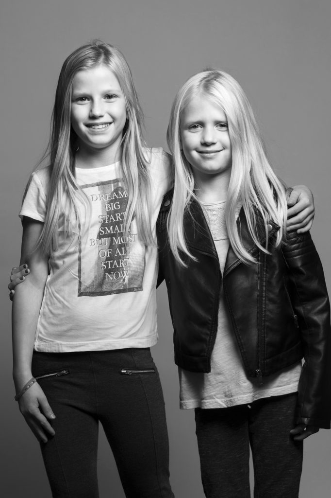 Verspieltes Familienportrait vom Fotostudio Reuther, das zwei Schwestern zeigt, die sich umarmen und in die Kamera lachen.