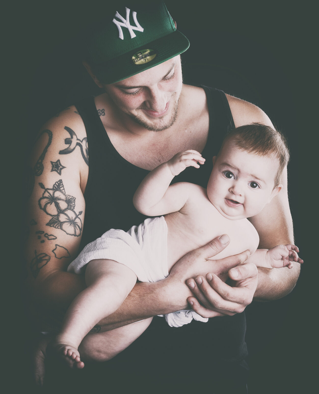 Zärtliches Familienportrait vom Fotostudio Reuther, das einen Vater zeigt, der sein Baby hält, während das Baby in die Kamera blickt.