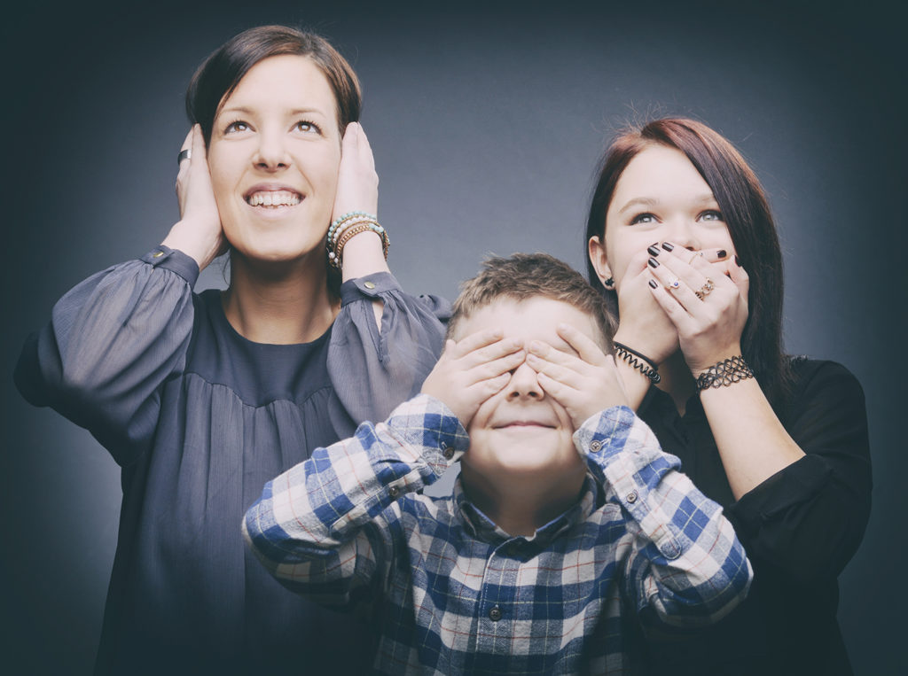 Lustiges Familienportrait vom Fotostudio Reuther, das eine Mutter und ihre Kinder in einer spielerischen Pose zeigt, während sie sich die Ohren, den Mund und die Augen zuhalten.