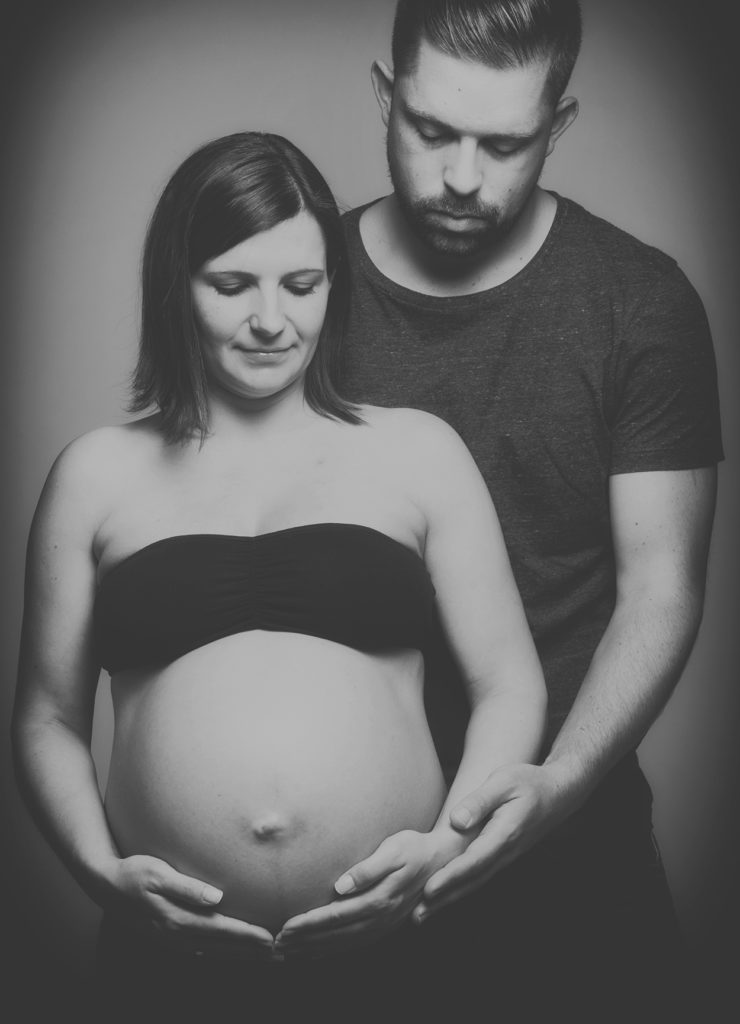 Ein Paar. Sie umarmen und betrachten den Bauch der Frau. Gestern noch schwanger - Schwangerschaftsfotografie eines Pärchens. Schwarz Weiß. Fotografiert von Fotostudio Reuther.