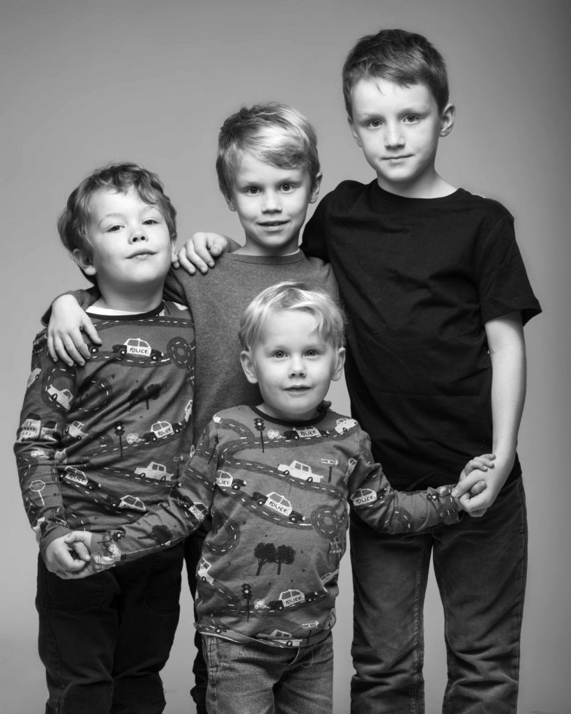 Verspieltes Familienportrait vom Fotostudio Reuther, das vier Brüder in einer lustigen Pose in Schwarz-Weiß zeigt.