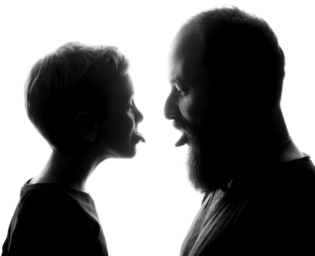 Verspieltes Familienportrait vom Fotostudio Reuther, das einen Vater und seinen Sohn zeigt, die sich gegenseitig die Zunge rausstrecken.