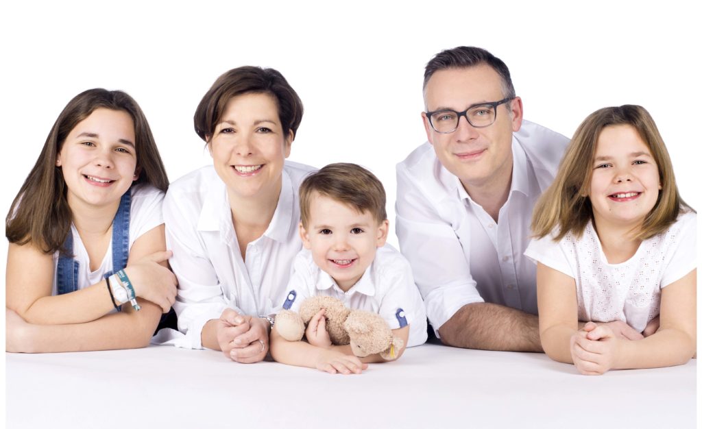 Lustiges Familienportrait vom Fotostudio Reuther, das eine Familie zeigt, die auf dem Bauch liegt und in die Kamera lacht.