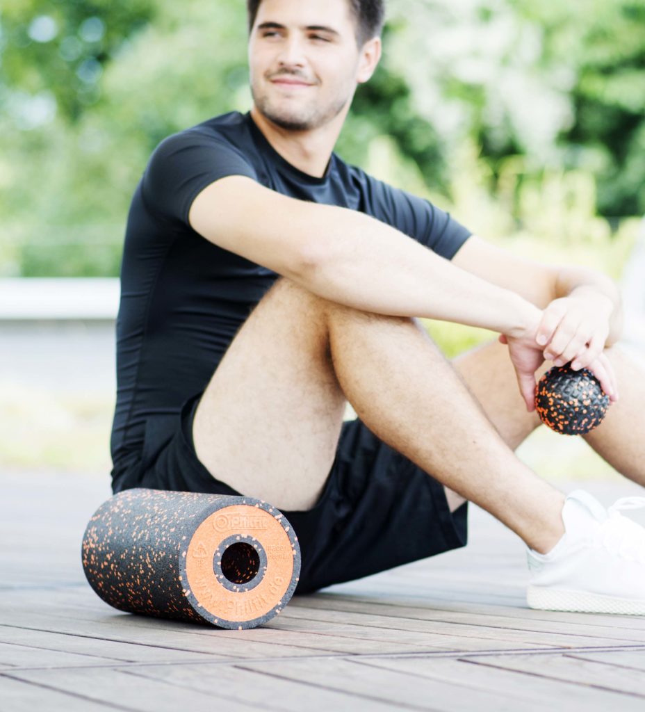 Portrait eines Mannes mit einer Faszienrolle, der entspannt und konzentriert aussieht, während er sich auf seine Regeneration und Fitness in einem ruhigen Yogastudio fokussiert.