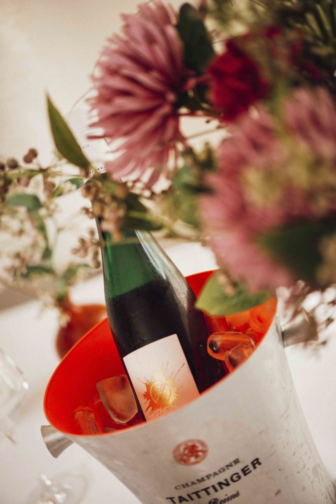 Detailaufnahme der Tischdekoration mit einer roten Blume und einer Flasche Wein im Kühler, die eine einladende Atmosphäre schafft.