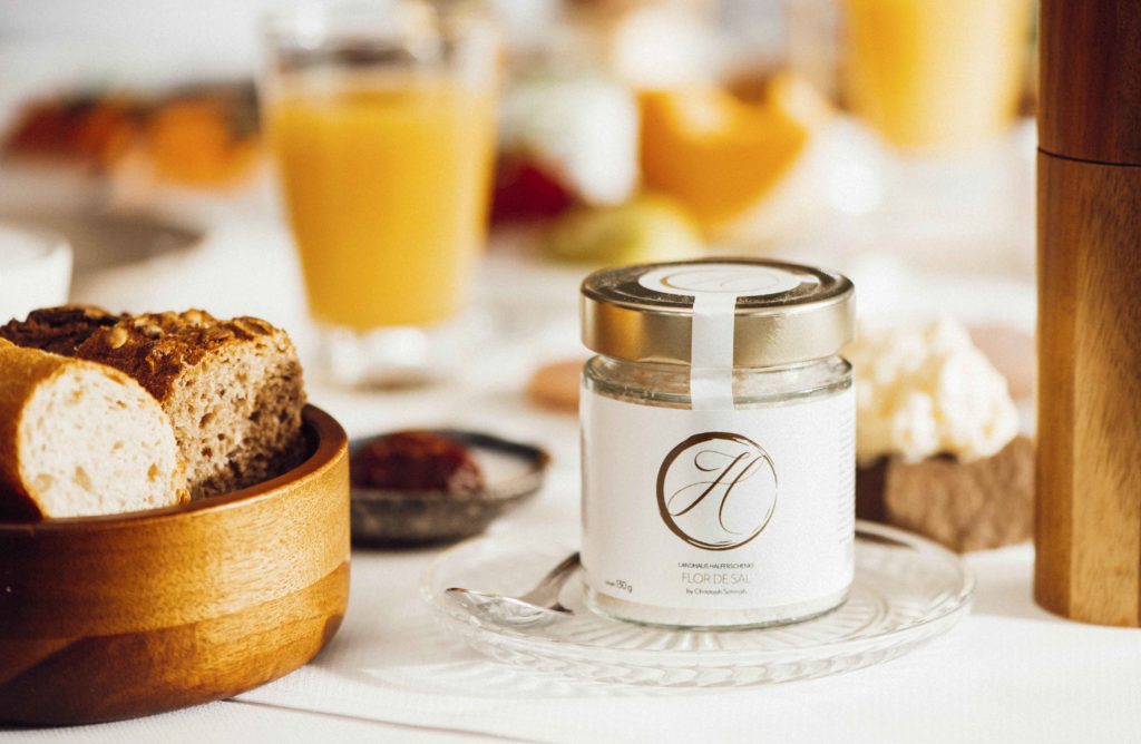 Detailaufnahme eines gedeckten Frühstückstisches im Hotel, der frische Brötchen, Brot, Obst und Saft präsentiert.