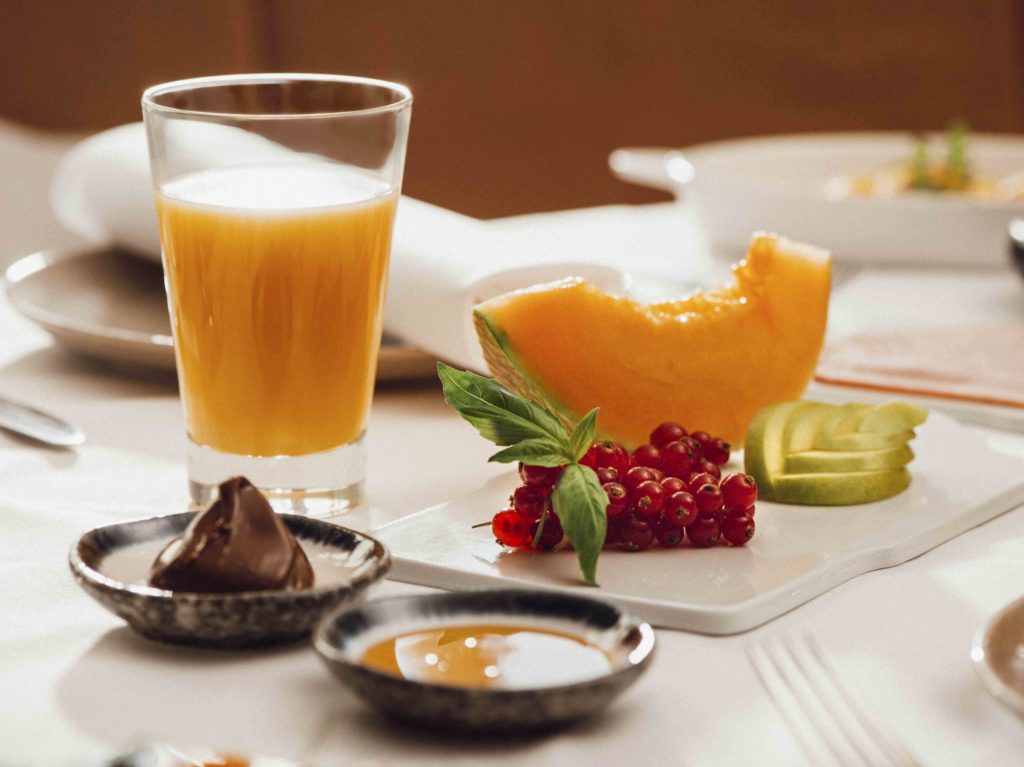 Detailaufnahme eines gedeckten Frühstückstisches im Hotel, der frische Brötchen, Brot, Obst und Saft präsentiert.