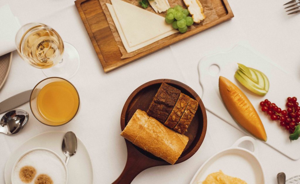 Detailaufnahme eines gedeckten Frühstückstisches im Hotel, der frische Brötchen, Brot, Obst und Saft präsentiert.