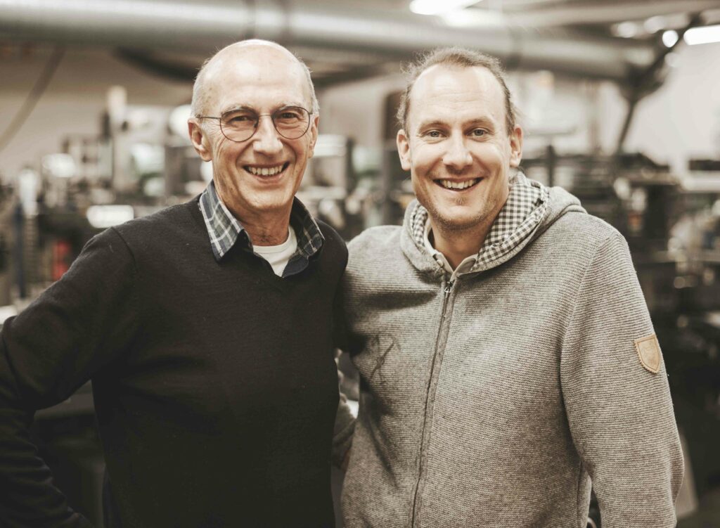 Portrait der Chefs der Etikettierfirma, lächelnd vor der Produktionsanlage.