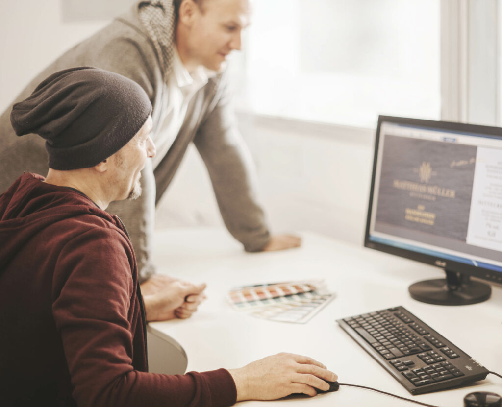 Leiter der Etikettierfirma im Gespräch mit einem Mitarbeiter am Computer, um Produktionsdaten zu überprüfen.