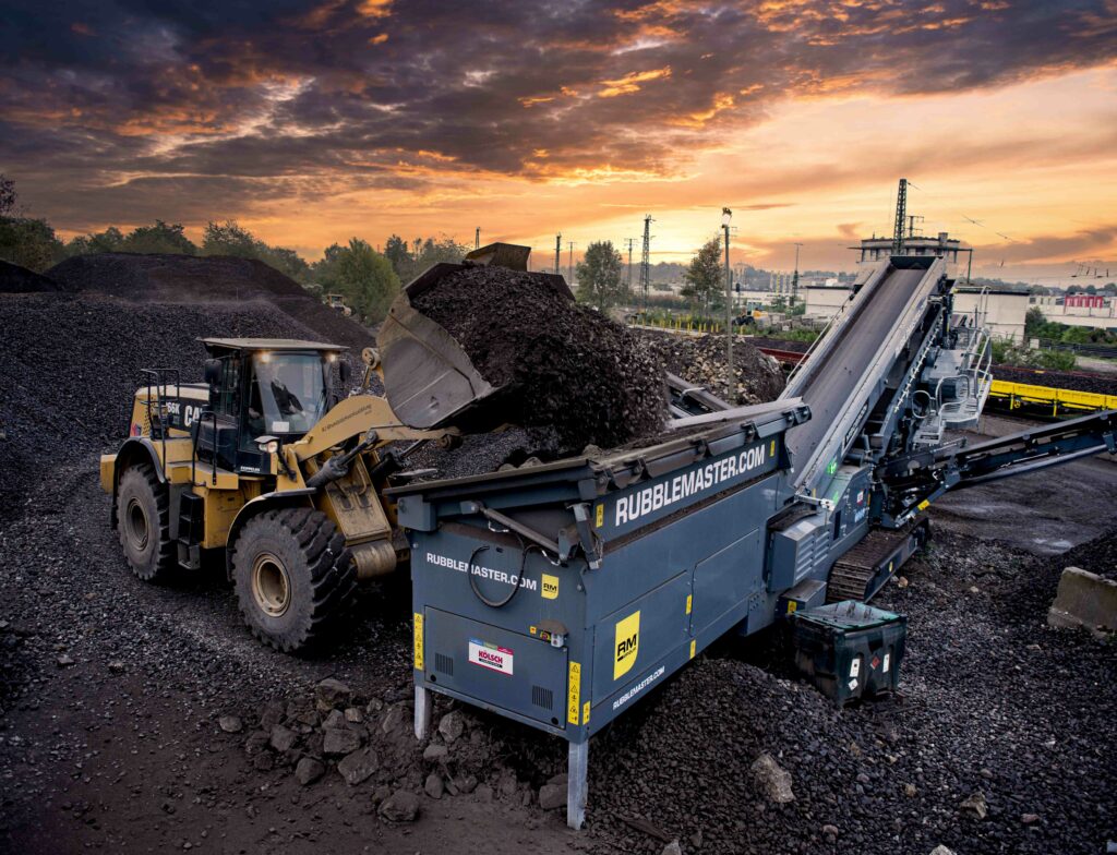 "Schottersortiermaschine bei Sonnenaufgang, die in warmes Licht getaucht ist und die ruhige Atmosphäre eines neuen Tages in einer industriellen Umgebung einfängt.