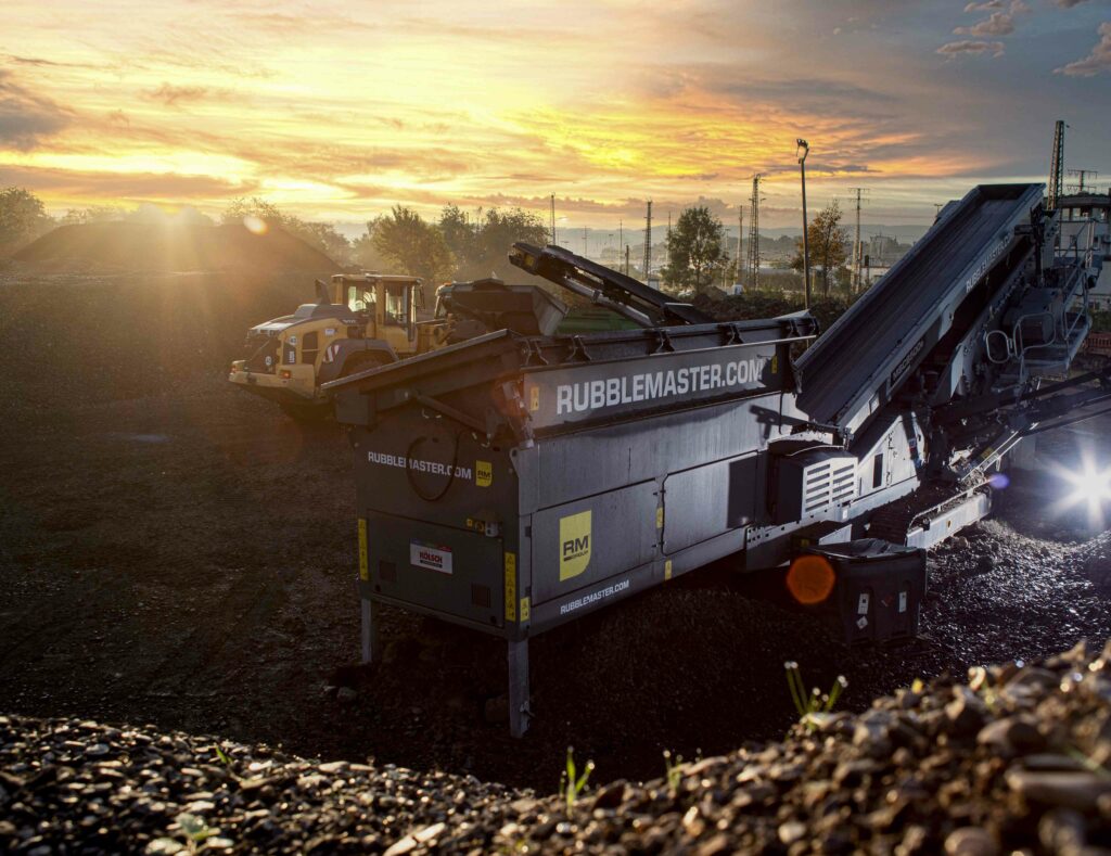 "Schottersortiermaschine bei Sonnenaufgang, die in warmes Licht getaucht ist und die ruhige Atmosphäre eines neuen Tages in einer industriellen Umgebung einfängt.