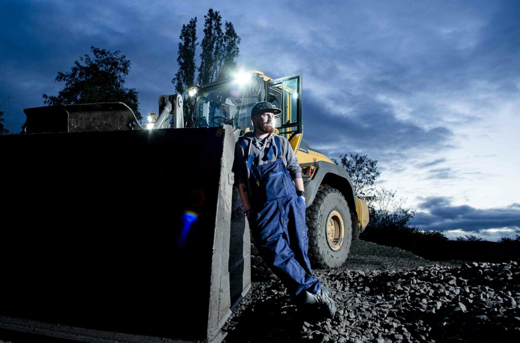 Bulldozer mit Arbeitern bei Nacht, die unter den Lichtern der Maschine an einem Bauprojekt arbeiten und eine dynamische Atmosphäre der nächtlichen Baustelle schaffen.