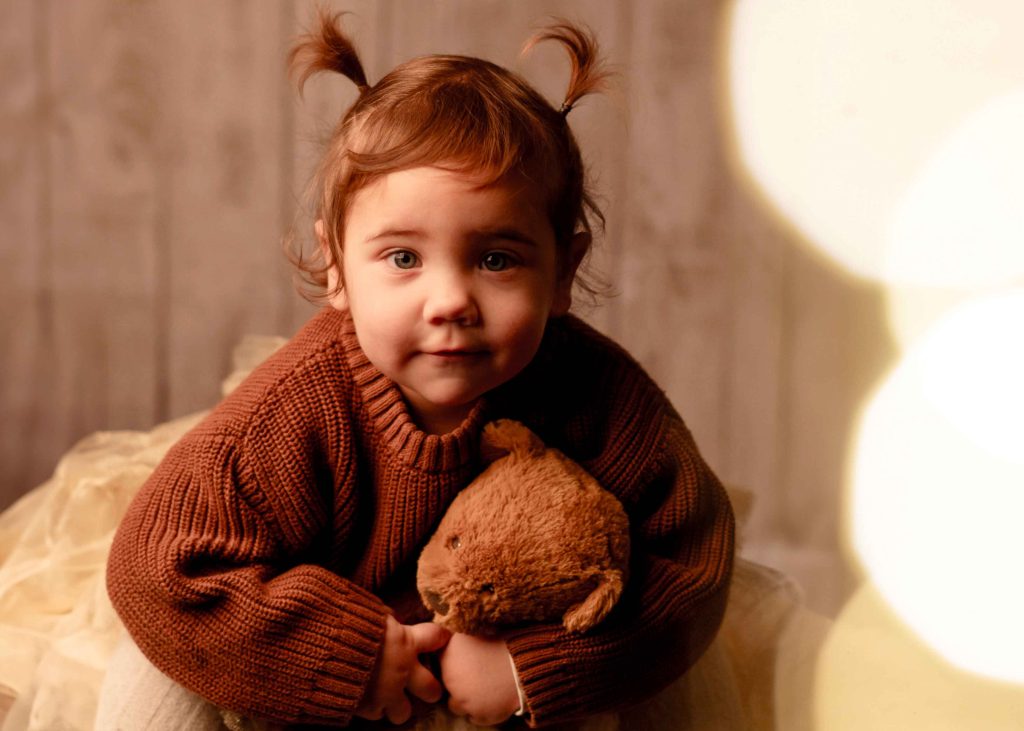 Verspieltes Familienportrait vom Fotostudio Reuther, das ein Mädchen mit ihrem Kuscheltier während eines Familienshootings zeigt.