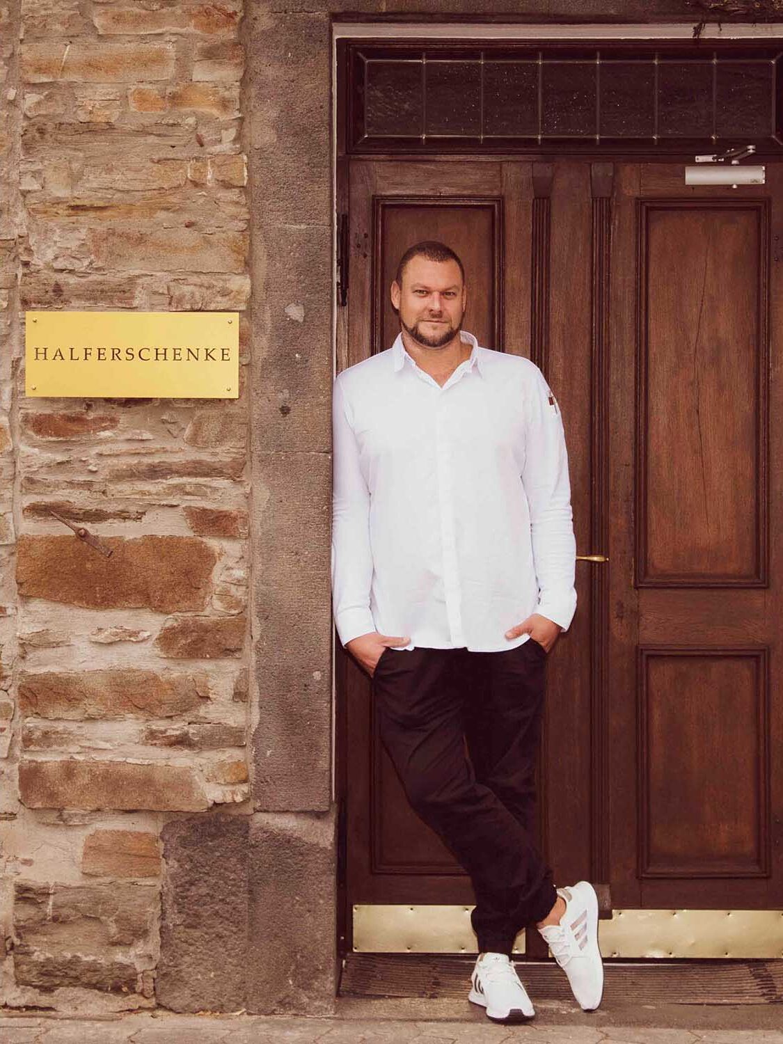 Küchenchef am Eingang seines Restaurants, der die Leidenschaft und Professionalität in der Gastronomiefotografie von Fotostudio Reuther repräsentiert.