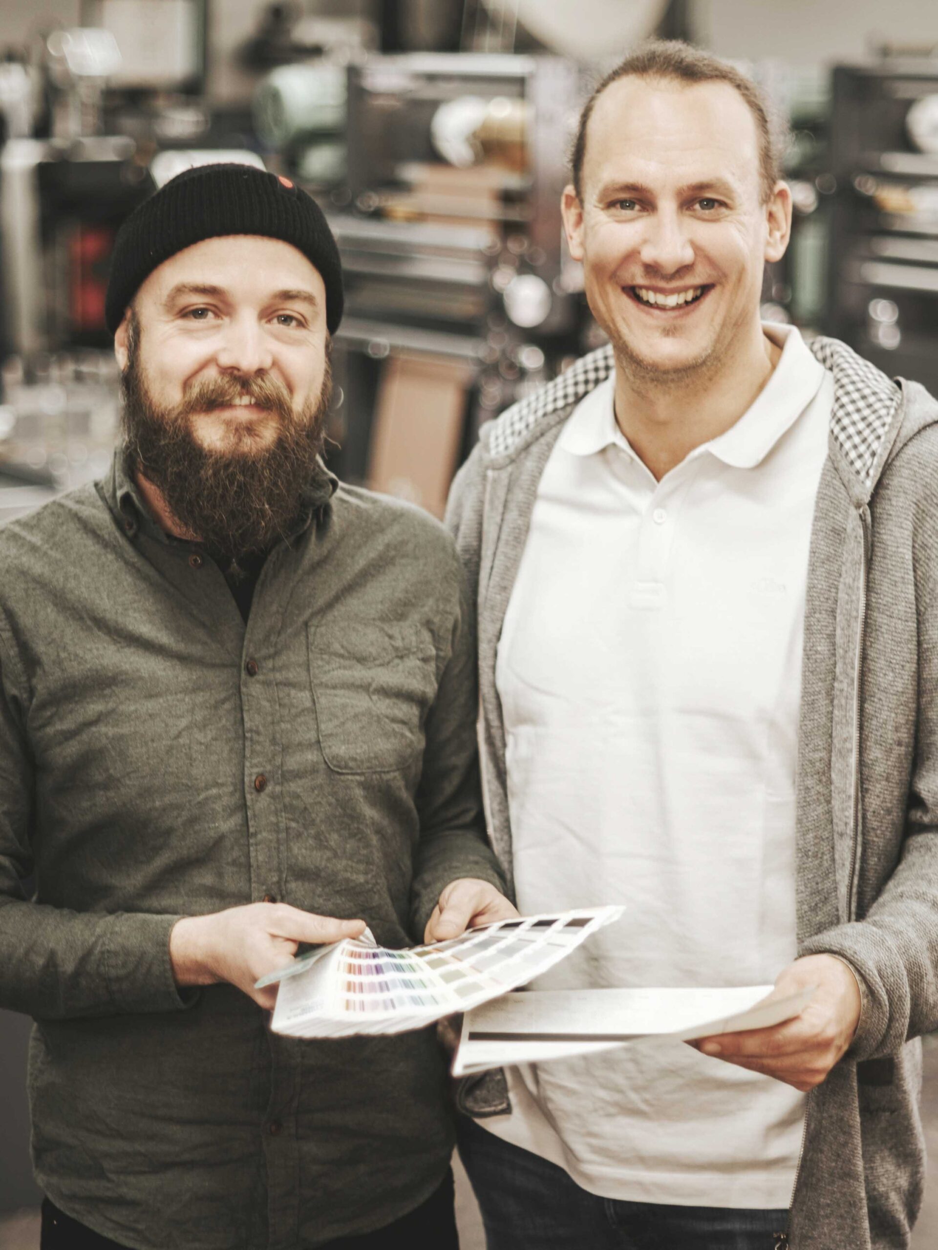 Portrait von Leiter und Mitarbeiter der Etikettierfirma vor dem Firmenhintergrund, lächelnd und professionell.